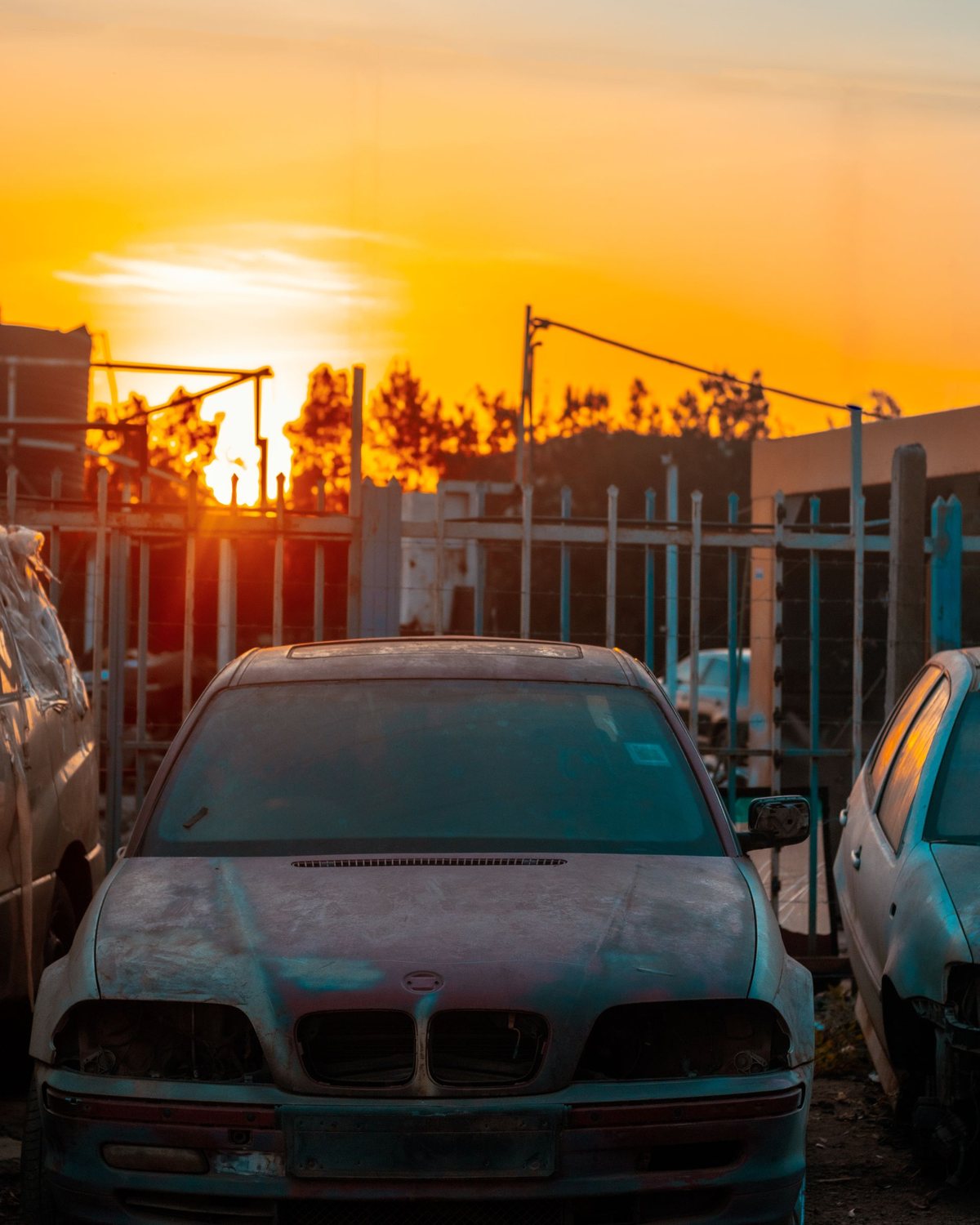 A junk car sitting in a salvage yard at sunset